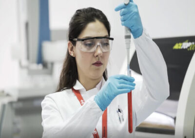 Female employee placing a red solution is a test tube wearing protective glasses and plastic gloves